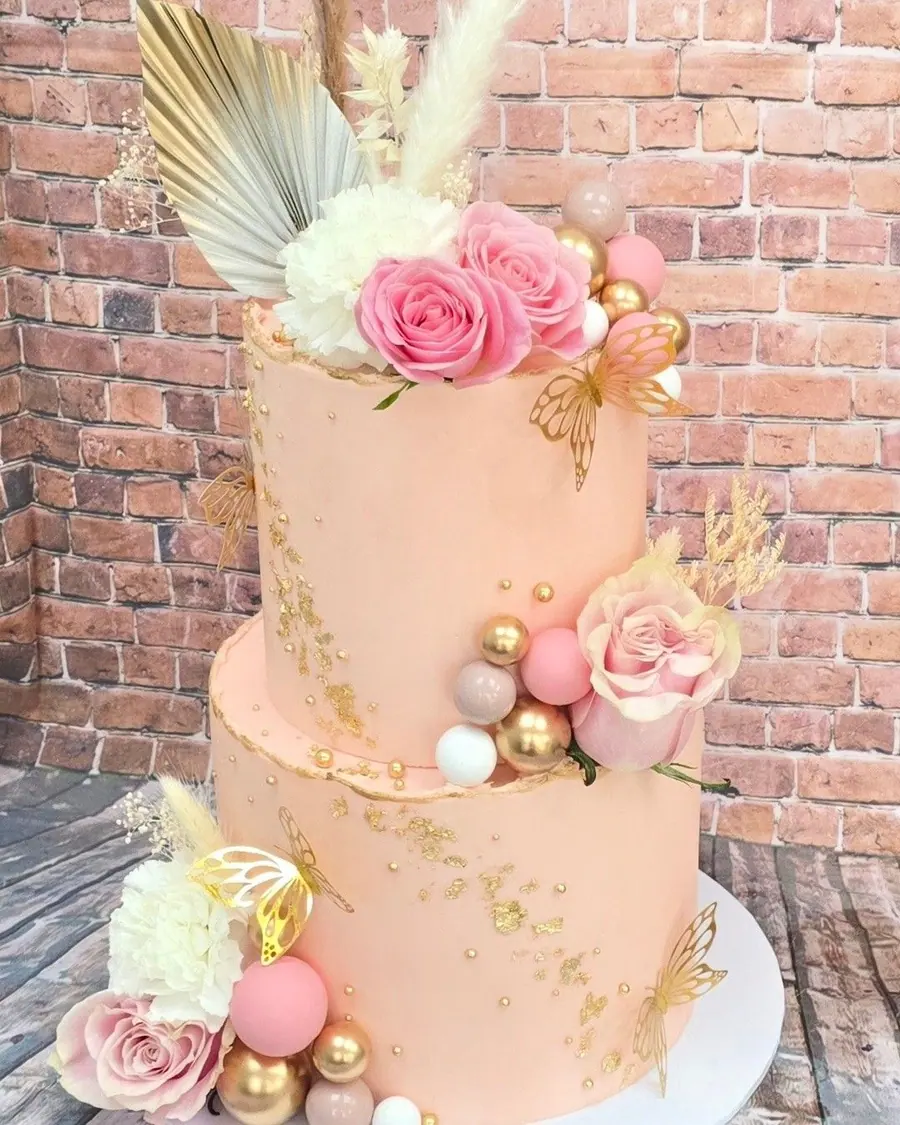 A tall pink buttercream cake with fresh flowers and gold details
